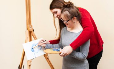 side-view-woman-helping-girl-with-down-syndrome-paint